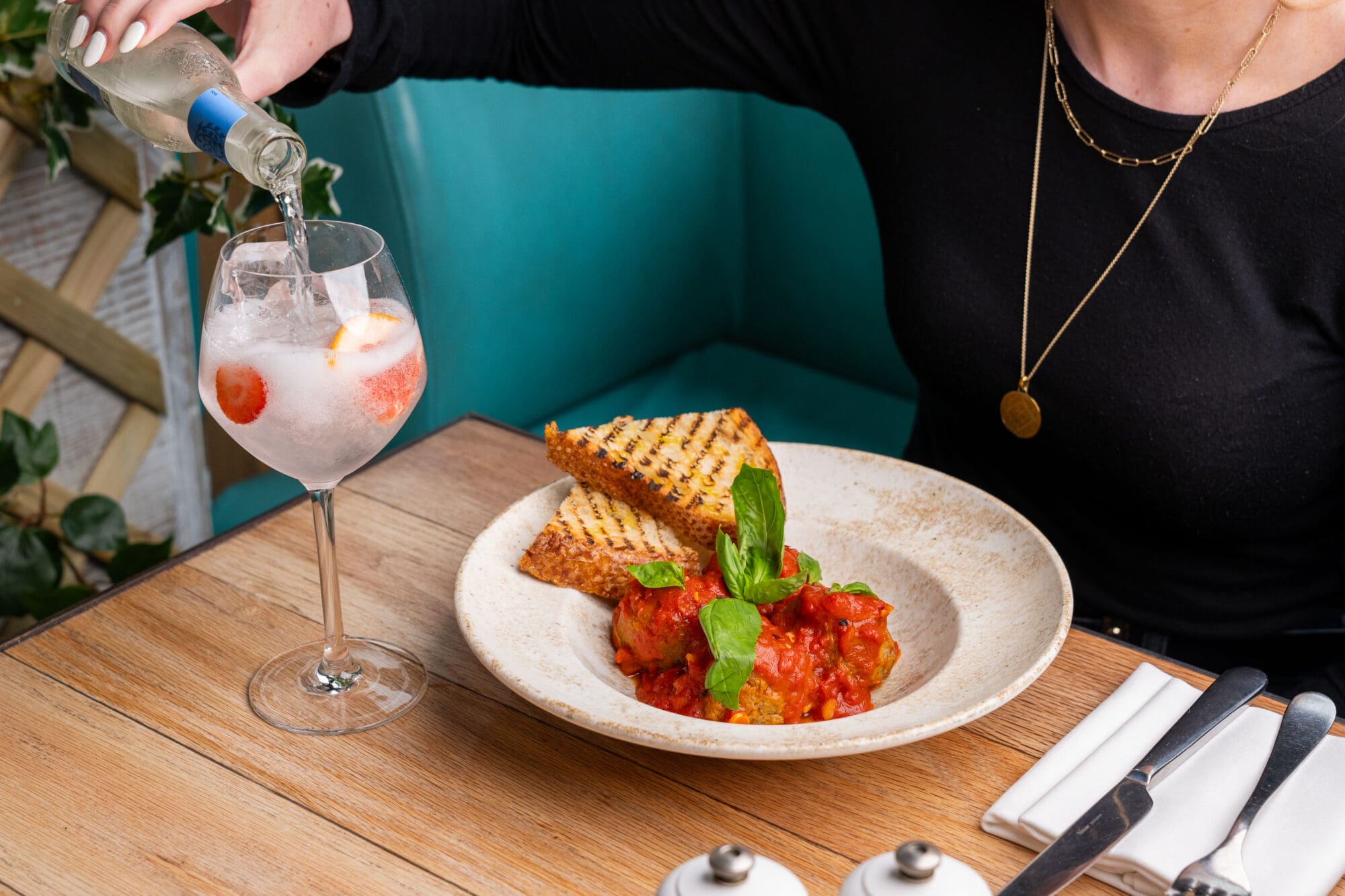 Woman is pouring tonic into a glass with a bowl of meatballs in front of her